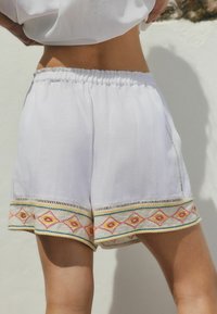 Vita shorts i lättviktsmaterial med färgglad geometrisk broderi längs fållen, med elastisk midja.