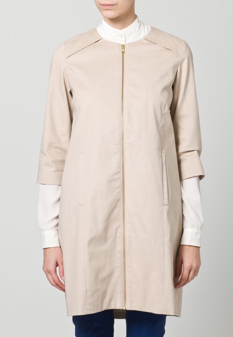 Vaaleanbeige trench-coat, jossa on vetoketjukiinnitys, kolmannen neljänneksen hihat, kaksi sivutaskua ja sileä pinta. Ominaisuuksiin kuuluu minimalistinen muotoilu.