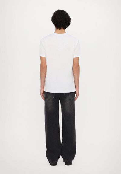 Weißes Kurzarm-T-Shirt mit rundem Halsausschnitt, kombiniert mit lockeren, ausgewaschenen schwarzen Jeans mit Gesäßtaschen und Nähdetails.