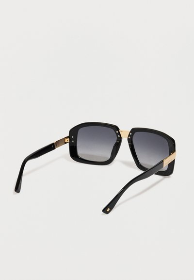 Occhiali da sole neri a forma quadrata con lenti scure sfumate e dettagli in metallo dorato sulle tempie e sul ponte su sfondo bianco.