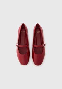 Par de zapatos planos Mary Jane rojos brillantes con punteras cuadradas y tiras con hebillas plateadas, con la marca Kate Spade New York en el interior.