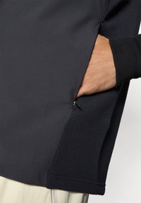 Black athletic pullover featuring a side pocket with mesh lining, smooth texture, and ribbed cuffs for comfort and functionality.
