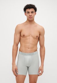 Lys grå boxertruser med en tettsittende passform. Har et elastisk midjebånd med "UNDER ARMOUR"-logo. Glatt, stretchy stoff og sømløst design.
