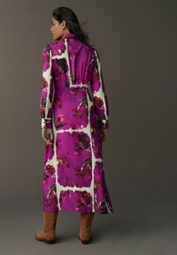 Rochie lungă cu mâneci, de culoare mov, cu un model floral alb, având o talie strânsă și un tiv până la gleznă, asortată cu cizme din suede maro.