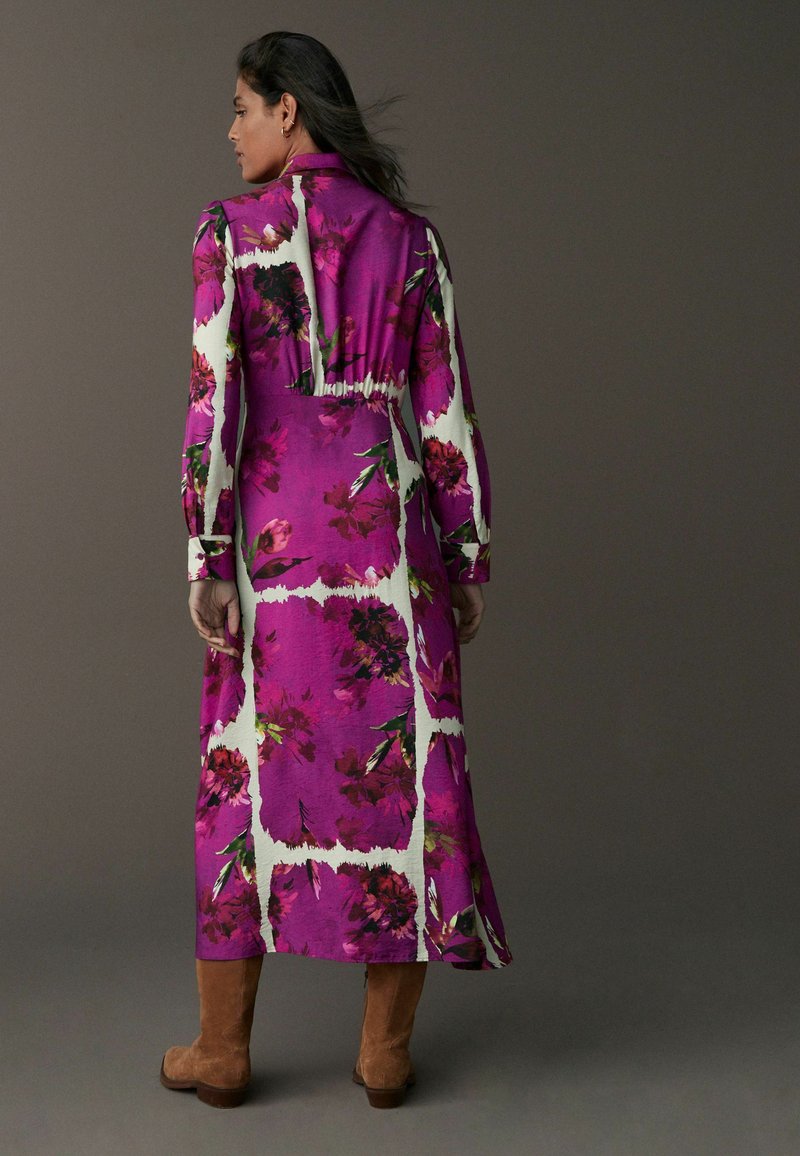 Rochie lungă cu mâneci, de culoare mov, cu un model floral alb, având o talie strânsă și un tiv până la gleznă, asortată cu cizme din suede maro.