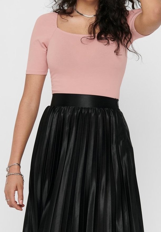 Haut ajusté rose clair à manches courtes associé à une jupe plissée noire taille haute en tissu brillant avec une ceinture élastique.