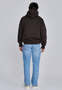 Mörkbrun hupptröja med lös passform, ihop med ljusblå jeans med raka ben. Enkel design med ribbade muddar och fåll.