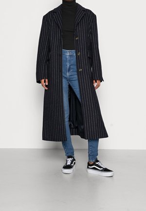 Marinfärgad randig kappa med slagkrage och tre knappar, som matchas med ljusblå högmidjade jeans och svarta sneakers.