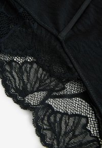 Gros plan sur un tissu en dentelle noire avec des motifs floraux et des bords festonnés sur un vêtement.