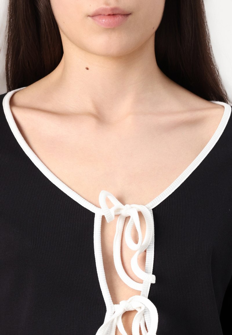 Top nero a coste con scollatura a V profonda e bordo bianco, dotato di un'apertura a chiave accentuata da due lacci al centro davanti.