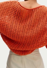Oranje, losgebreid truitje met een ruime halslijn en geribde zoom. De textuur is open en luchtig, met een mix van ingewikkelde patronen.