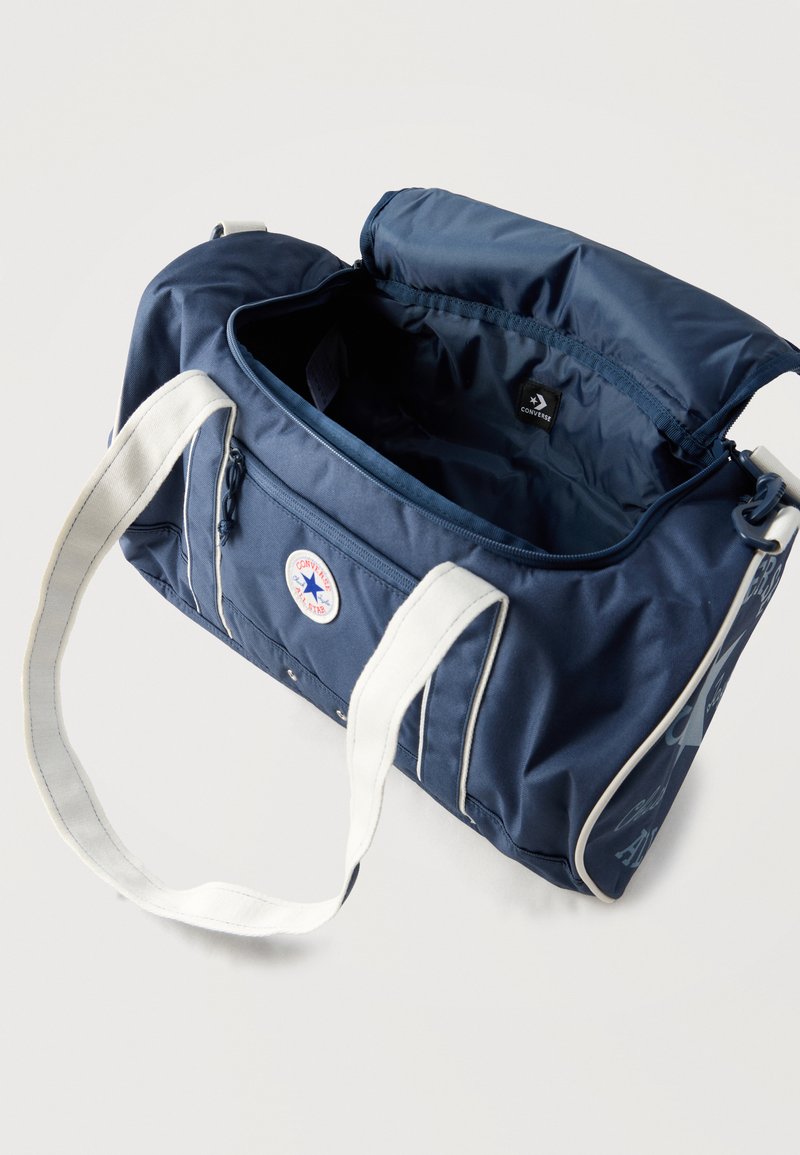 Marineblaue Converse-Weekender-Tasche mit weißen Griffen, offenem Reißverschluss oben und sichtbarem Innenraum mit Markenetikett.