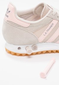 Světlé šedé tenisky z semiše a síťoviny s růžovými akcenty a třemi proužky. Mají odnímatelné hroty a gumovou podrážku s protiskluzovou úpravou.