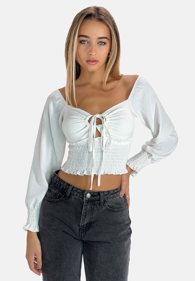 Haut blanc court avec des manches bouffantes, devant froncé avec des cordons de serrage. Associé à un jean noir taille haute pour une silhouette ajustée.