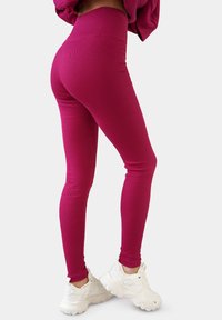 Aansluitende, geribbelde legging in een levendige magenta kleur met een hoge taille. Gepaard met witte sport sneakers, met een gladde textuur.