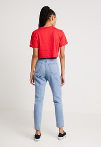 Camiseta corta roja combinada con jeans de tiro alto azul claro; zapatillas negras completan el atuendo casual. Cabello peinado en trenzas.