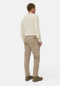 Beige corduroy cargo bukser med sidelommer, parret med en cremefarvet langærmet skjorte og brune ankelstøvler. Ensfarvet baggrund.
