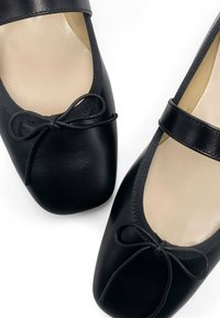 Bailarinas de cuero negro con punta redondeada, que cuentan con un lazo decorativo en el empeine y un forro beige suave.