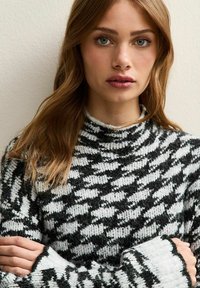 Zwart-wit gebreide trui met een hoge halslijn en lange mouwen, met een zachte, gestructureerde afwerking en een losse pasvorm.