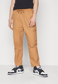 Beige cargobyxor med resår i midjan och dragsko. Har sidoficka, avsmalnande passform och bärs med svartvita höga sneakers.