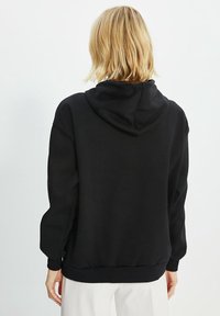Sweat-shirt noir à capuche, avec une coupe décontractée et des poignets et ourlet côtelés. Texture douce, design minimaliste sans logos ni motifs visibles.