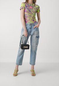 Barevné tričko s tie-dye vzorem v zelené, fialové a žluté barvě; světle modré cargo džíny; černá kabelka se zlatým logem; zelené sandály na řemínky.