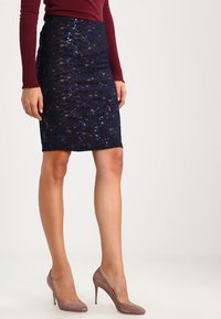 Marinblå paljettpennkjol med ett strukturerat spetsmönster, i kombination med ljusrosa mockahögklackade skor. Kjolen är knävitt och figurnära.