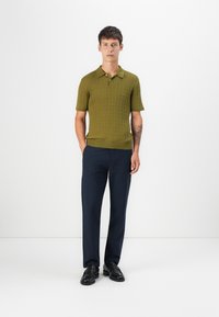 Oliven grøn strikket polo med ribbet struktur, korte ærmer og krave. Sammen med marineblå bukser og sorte loafers.