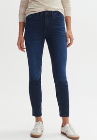 Dunkelblaue Skinny Jeans aus Denim, mit einer Hüfthöhe in der Mitte, Five-Pocket-Design und einer glatten Textur. Tragen mit weißen Sneakers.