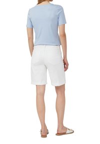 Haut à manches courtes bleu clair porté avec un short bermuda en denim blanc, présentant des ourlets roulés et des poches arrière, associé à des sandales claires.