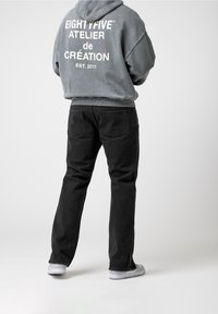 Vaqueros de mezclilla negros combinados con una sudadera con capucha gris que tiene texto blanco en la parte trasera. El conjunto tiene un ajuste relajado y un estilo casual.