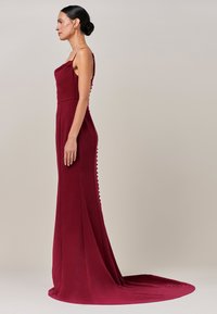 Vino crvena večernja haljina s uskim korzetom, tankim naramenicama i dugom suknjom s vlakom te detaljima s gumbima na stražnjoj strani.