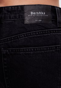 Vaqueros de mezclilla negros con una cinturilla texturizada que lleva una etiqueta de "Colección de Denim de Bershka", costuras destacadas y un diseño de bolsillo clásico.