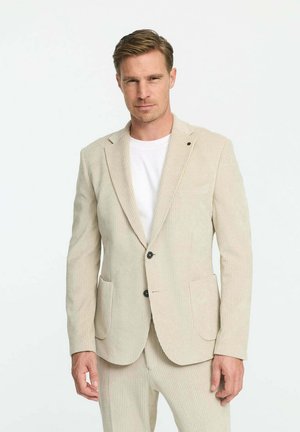 Beige Corduroy-Blazer mit Revers, zwei Taschen vorne, zwei Knöpfen und dezenten vertikalen Streifen; getragen über einem weißen T-Shirt.
