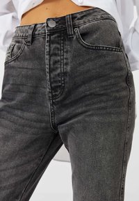 Musta denim-farkut, joissa on korkea vyötärö, nappi- ja vetskarempu, etutaskut ja hieman haalistunut pinta.