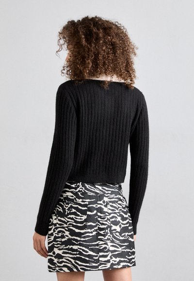 Μαύρο ριγωτό πουλόβερ με μακρυά μανίκια, συνδυασμένο με μια φούστα ψηλόμεση που έχει μοτίβο ζέβρας σε μαύρο και λευκό χρώμα.