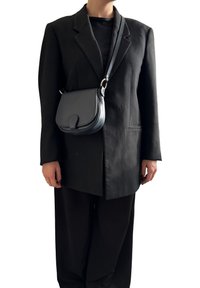 Borsa a tracolla in pelle nera con una forma curva, dotata di chiusura a patta e hardware in tonalità argento. Indossata con un blazer nero oversize.