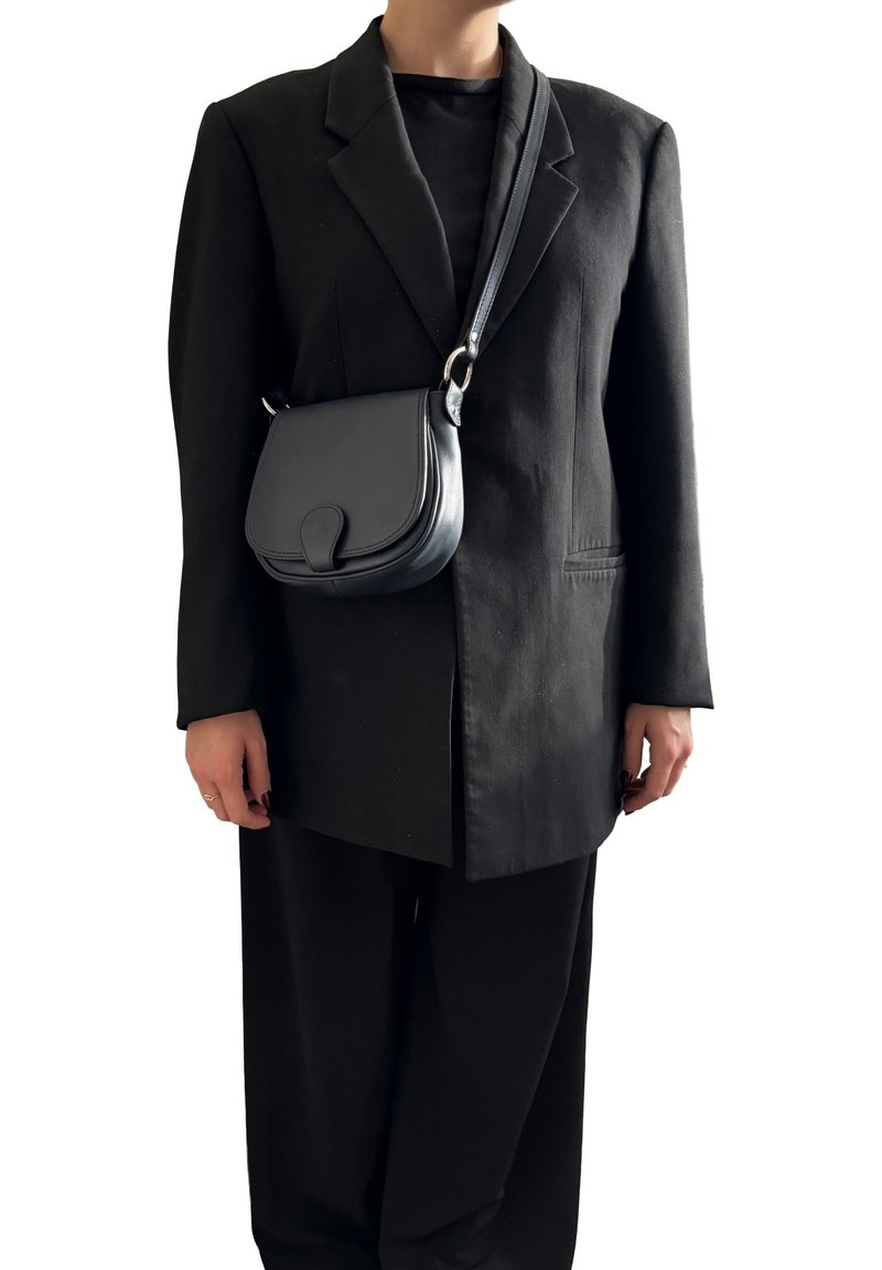 Borsa a tracolla in pelle nera con una forma curva, dotata di chiusura a patta e hardware in tonalità argento. Indossata con un blazer nero oversize.