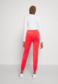 Velvet joggers i ljus korall, med en smal passform, elastisk midja och vita sidobårder. Matching med en åtsittande vit långärmad topp.