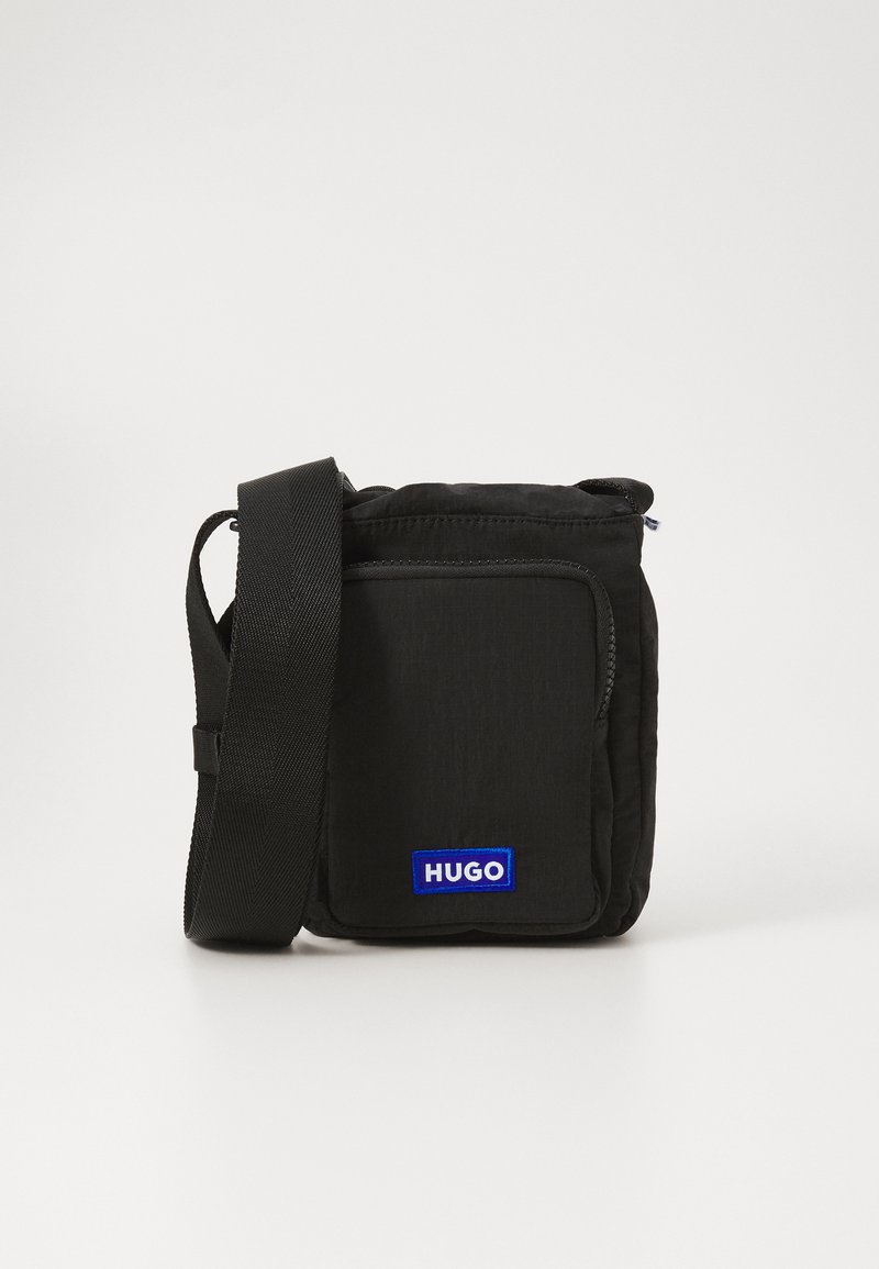 Svart crossover-veske laget av teksturert nylon, med en frontlomme og et blått "HUGO" logo-patch. Justerbar stoffrem for enkelhet.