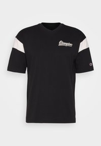 Camiseta negra de cuello en V hecha de algodón, con rayas blancas en las mangas y un logo de Champion en el pecho. Mangas cortas, ajuste casual.