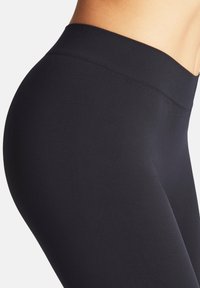 Leggings noirs avec une taille haute, une texture lisse et une coupe ajustée, présentés de profil.
