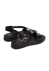 Sandales en cuir noir avec des lanières croisées, des accents en métal argenté et une semelle rembourrée avec une légère plateforme pour le confort.