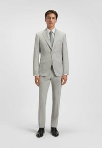 Jasnoszary garnitur dopasowany, z jednorzędową marynarką, klapami w kształcie notcha, dwiema przednimi kieszeniami oraz spodniami prostymi. W zestawie z białą koszulą i krawatem.