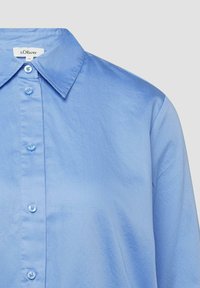 Chemise boutonnée bleu clair avec col pointu, comportant une étiquette de marque s.Oliver et une taille 36 à l'intérieur du col.