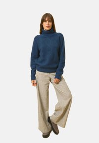 Námorně modrý rolák se strukturovaným diamantovým vzorem, zkombinovaný se světle šedými kalhotami s širokými nohavicemi a černými platformovými botami.