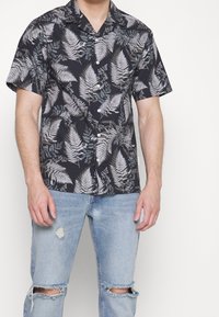 Korte mouwen, donkerblauwe shirt met lichtgroene en witte varenpatronen, knoopsluiting, gemaakt van lichte stof, gecombineerd met gescheurde lichtblauwe jeans.