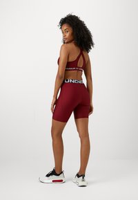 Soutien-gorge de sport rouge et short assorti, fabriqués en tissu lisse. Présente un design dos nageur et une taille élastique avec un logo. Baskets noires et blanches.