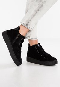 Mustat mokkasiinilätsät, joissa on tekstiuri ja koristeelliset vetoketjut, nauhakiristys sekä sileä musta kantakuppi.