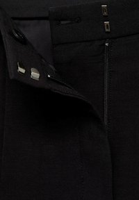 Czarne spodnie wykonane z gładkiego materiału z suwakiem, połączone z zapięciem na guziki i metalowymi akcentami. Widać wyraźne detale szwów.